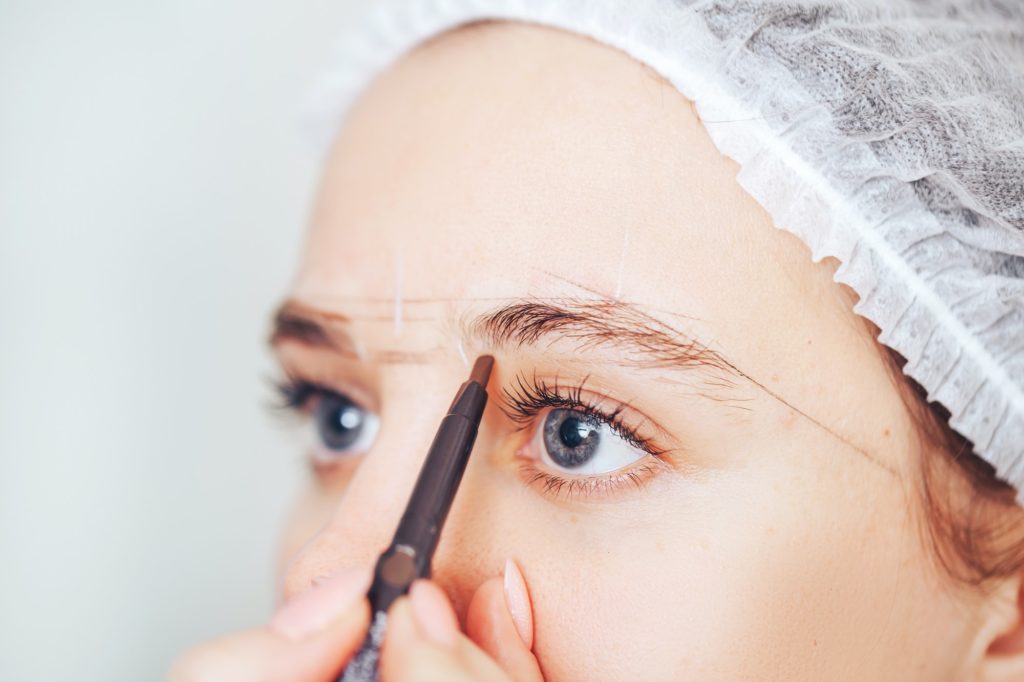 Cosmetolog beauty master making marks with pencil before the permanent makeup procedure